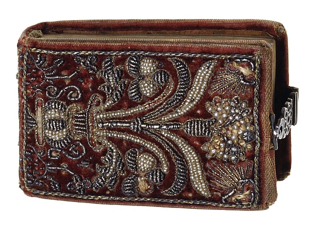 Front cover of a small, old book with red velvet binding. The binding is elaborately embroidered with silver beads. The embroidery depicts flowers in a vase.