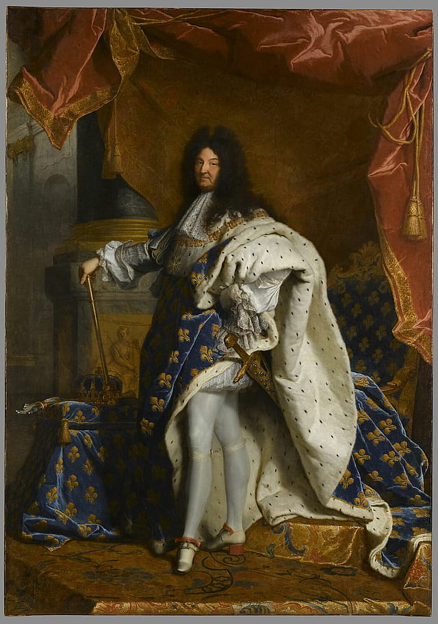 Full-length painting of a king. He is wearing an elaborate, long silk and fur coat with a blue pattern over white tights. He has long, black, curly hair and is holding a cane. Behind him there is a large red and yellow curtain and a pillar.