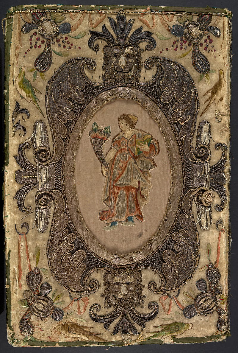 Back cover of an old book with embroidered binding. The binding depicts a full-length female figure within a cartouche. She has brown hair and is wearing a red and white flowy dress and gold cap. She is holding a cornucopia filled with wheat or grains. Lion heads decorate the top and bottom of the cartouche. Around the cartouche are decorative embroidered floral designs.