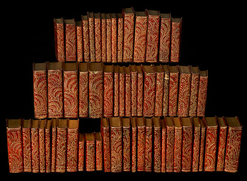 Fifty-nine travel-sized books grouped together. Each book has red binding with gold decoration.