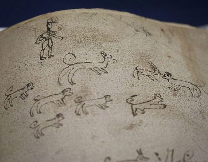 Close-up detail of page from an old book with a doodle in ink of a pack of dogs and a man with a cap.