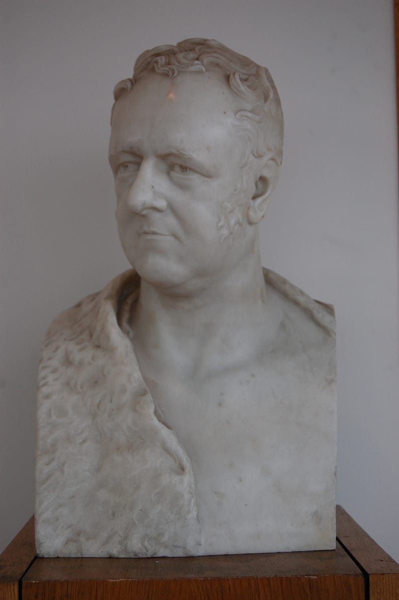 Photograph of a marble bust of an older gentleman with short, wavy hair. He appears to be wearing a fur shawl.